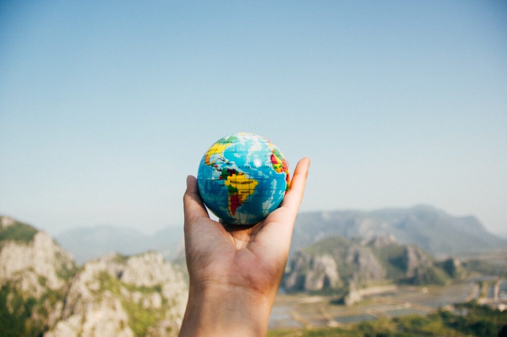 Hand holding a small globe in front of a landscape